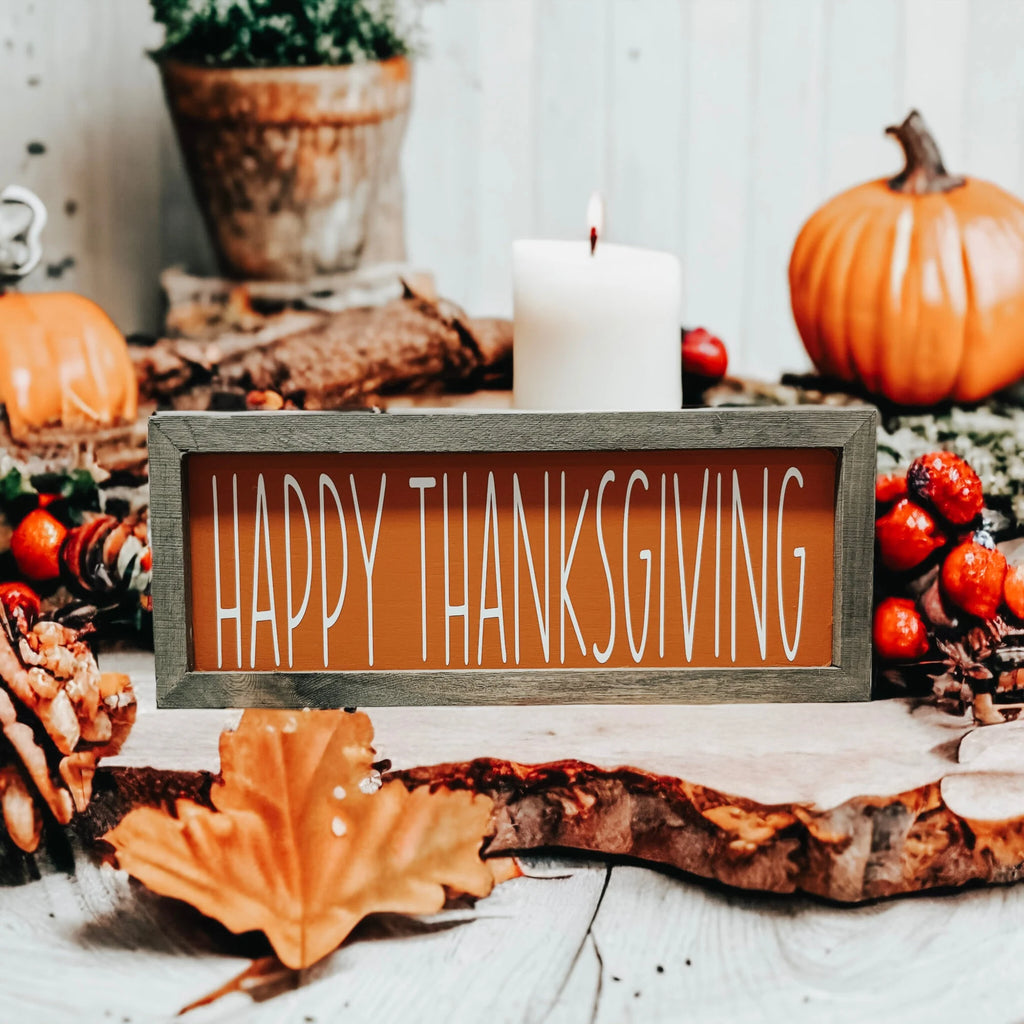 Rustic Happy Thanksgiving orange wood sign with grey frame on white wood table with woven baskets and orange pumpkins