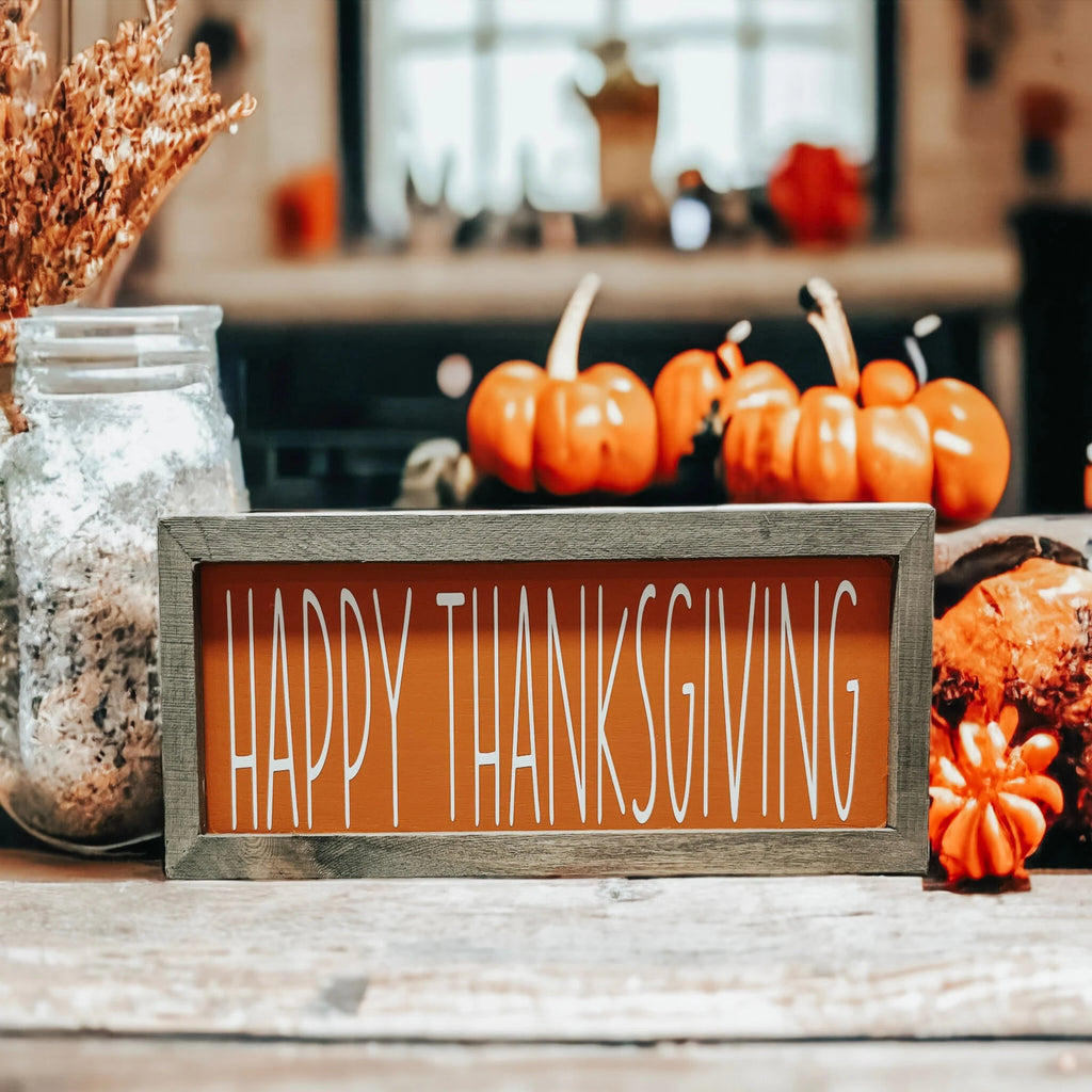 Rustic Happy Thanksgiving orange wood sign with grey frame on white wood surface with candles and fall leaves warm bokeh background
