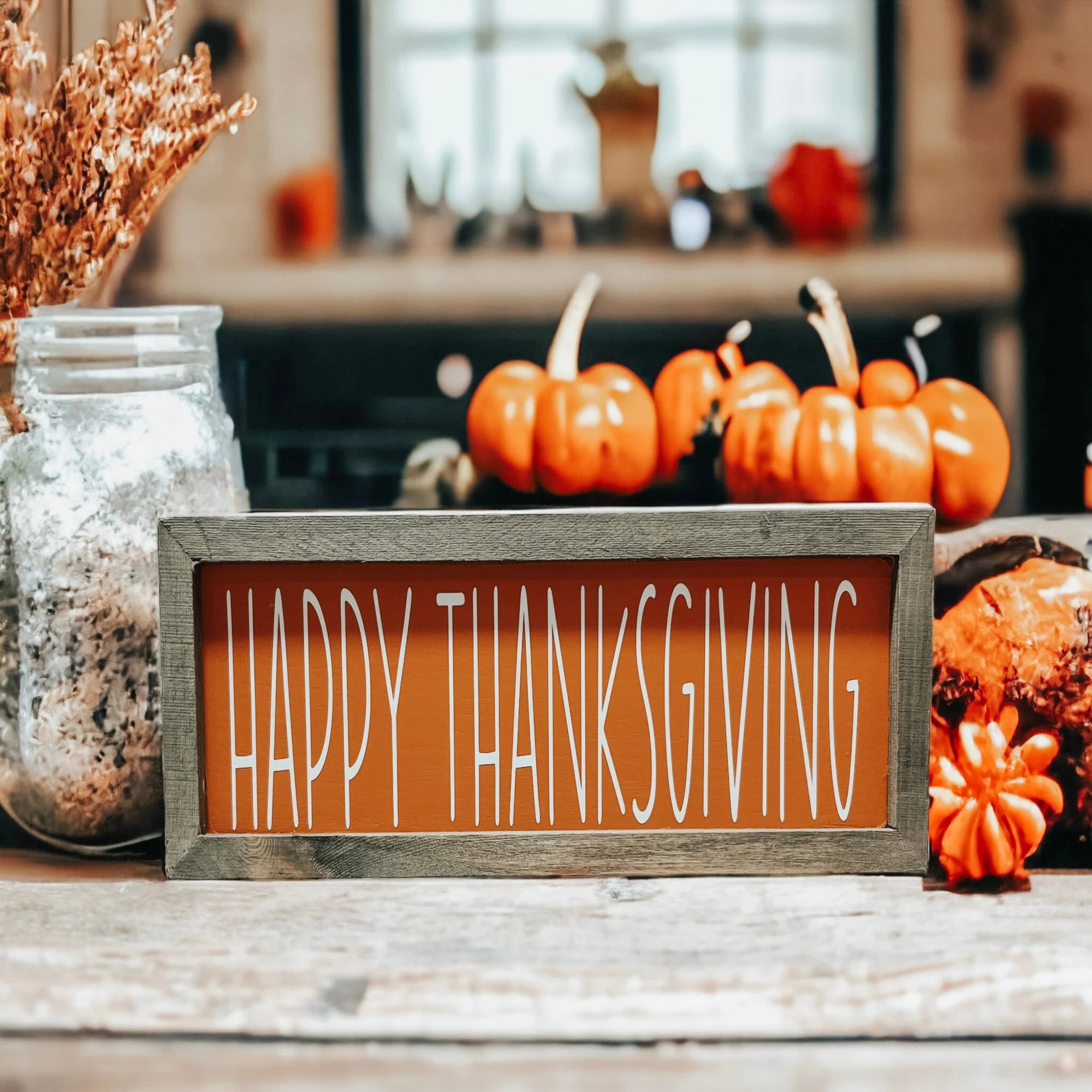 Rustic Happy Thanksgiving orange wood sign with grey frame on white wood surface with candles and fall leaves warm bokeh background