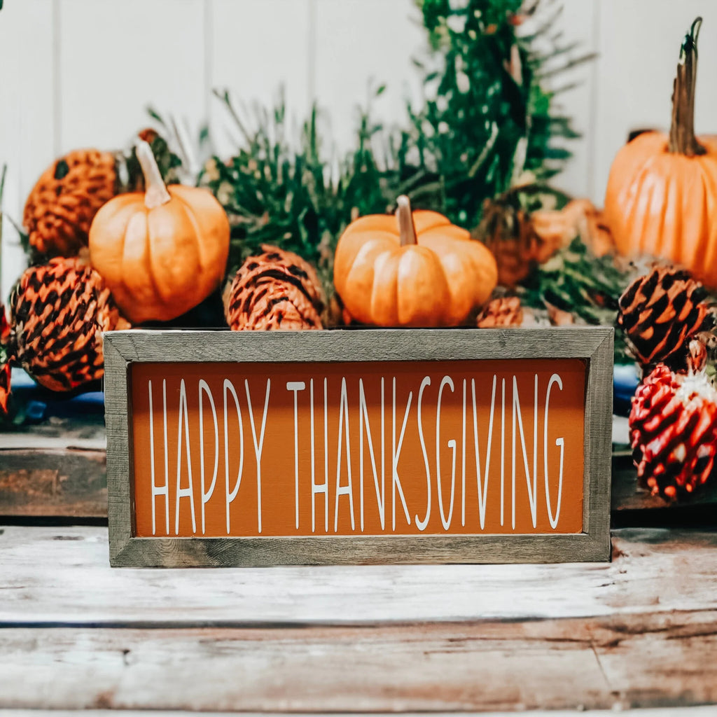 Rustic Happy Thanksgiving orange wood sign with grey frame on white wood surface with dried botanicals and orange pumpkins wide shot