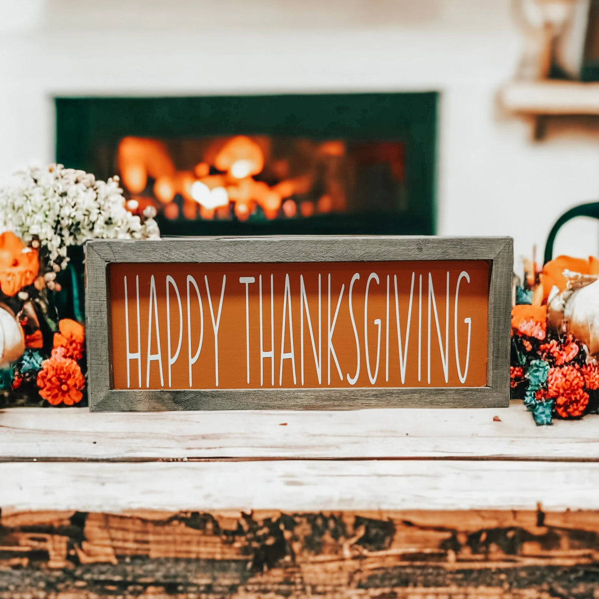 Rustic Happy Thanksgiving orange wood sign with grey frame on white wood surface with orange pumpkins and woven basket close up