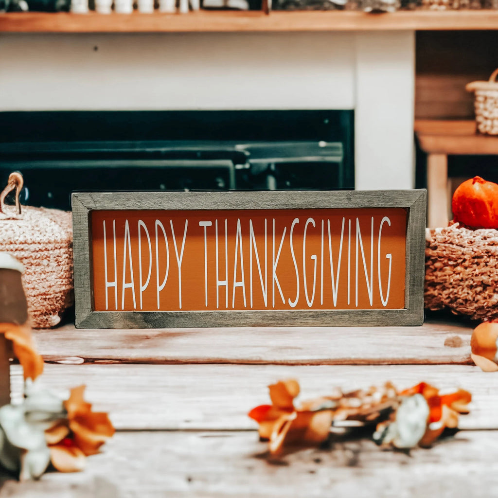Rustic Happy Thanksgiving orange wood sign with grey frame on white wood surface with mason jar and orange pumpkins in kitchen