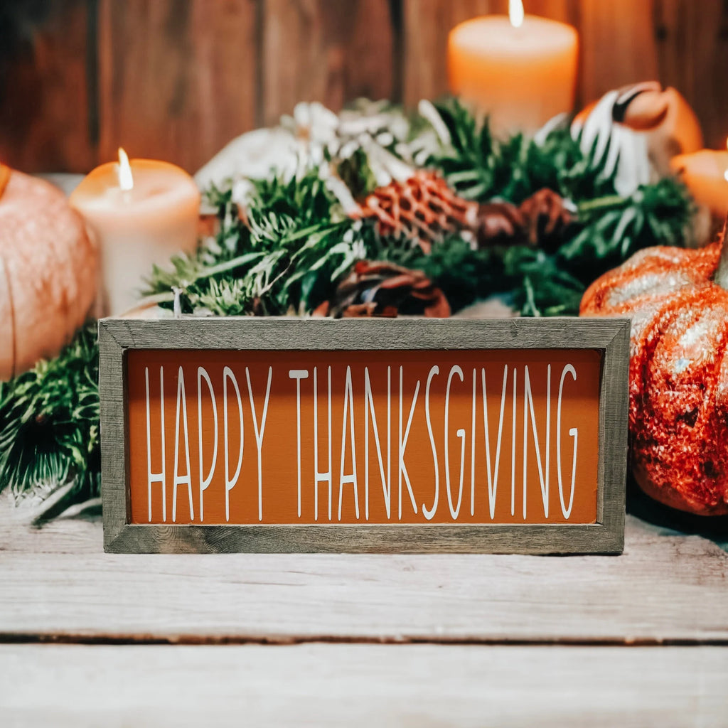Rustic Happy Thanksgiving orange wood sign with grey frame on white wood surface with orange pumpkins and pine cones fall display