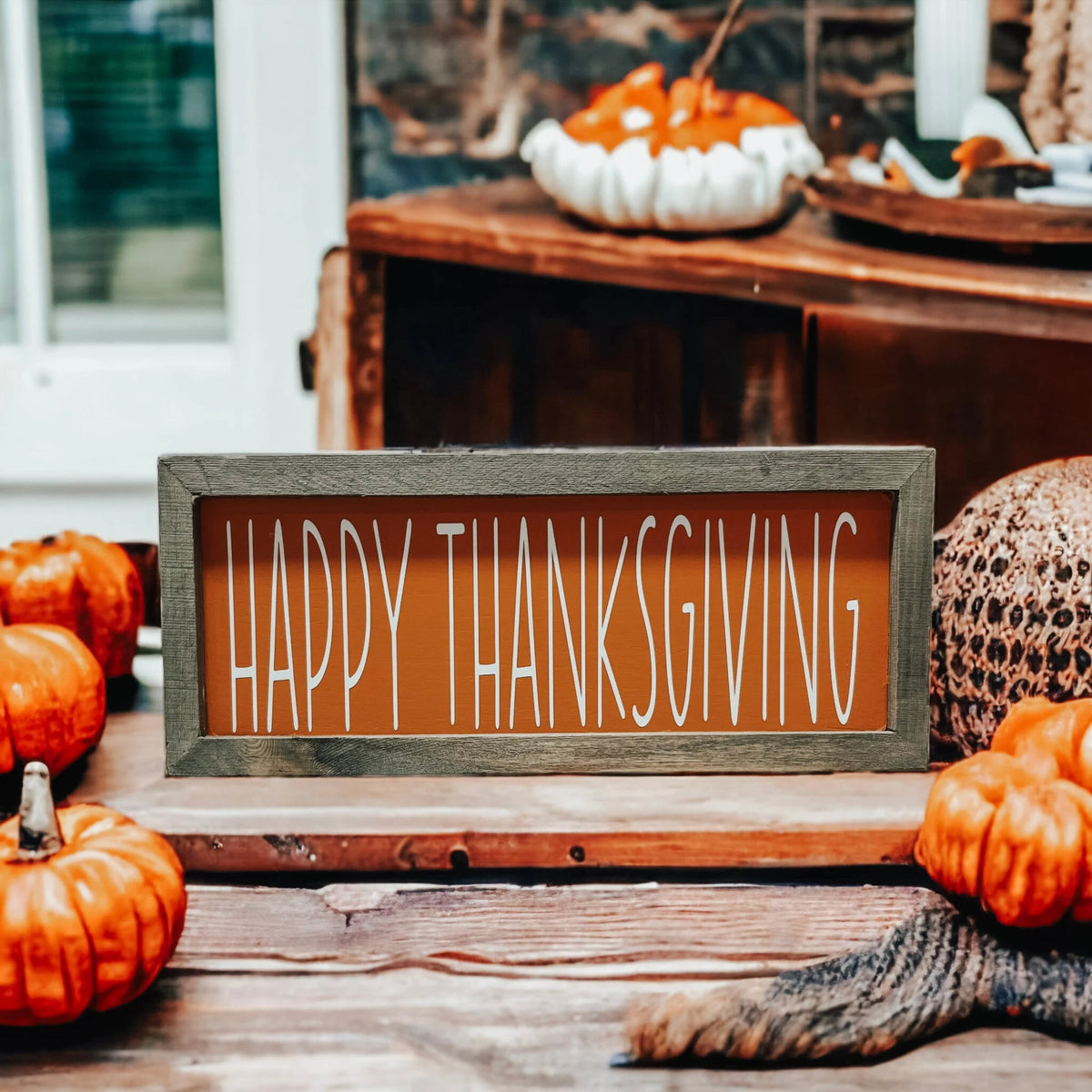 Rustic Happy Thanksgiving orange wood sign with grey frame on wood slice with dried botanicals and orange pumpkins on kitchen counter