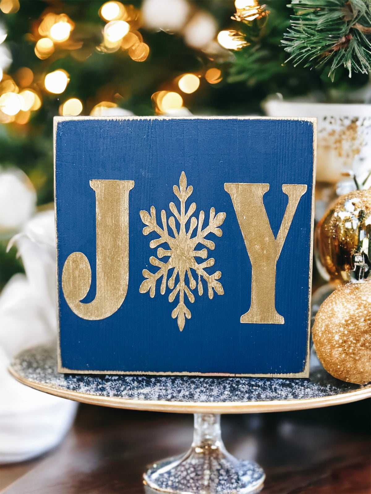 JOY navy blue Christmas wood block sign with gold serif J and Y and gold snowflake O product hero shot on white background