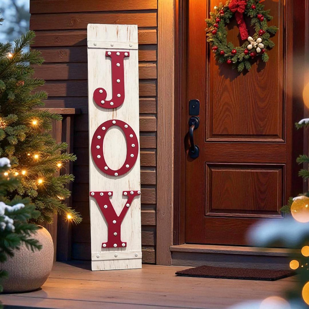 JOY porch leaner sign with red marquee letters leaning against red front door with Christmas trees in red pots