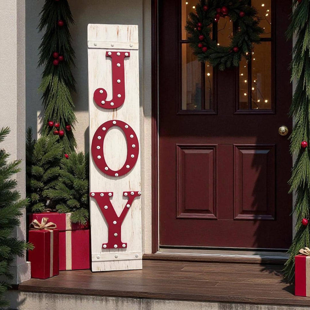 JOY porch leaner sign with red marquee letters leaning against dark red front door with Christmas wreath and red bow