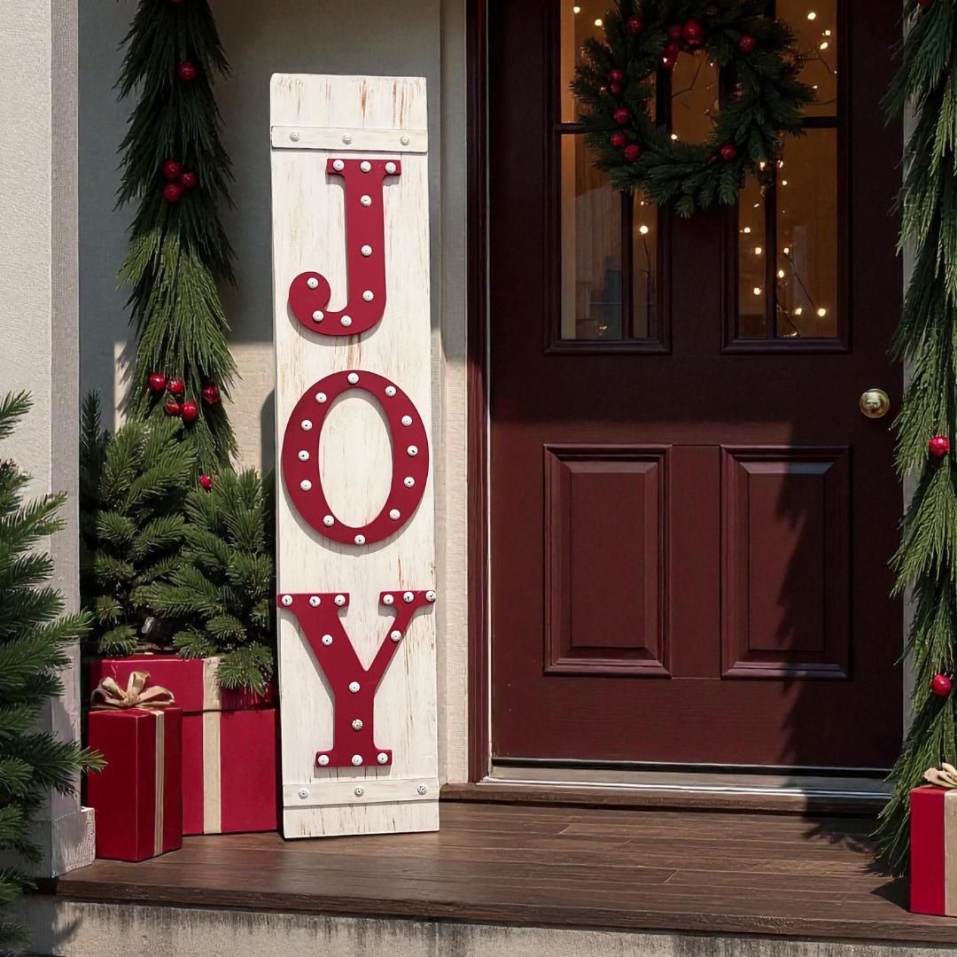 JOY porch leaner sign with red marquee letters leaning against dark red front door with Christmas wreath and red bow