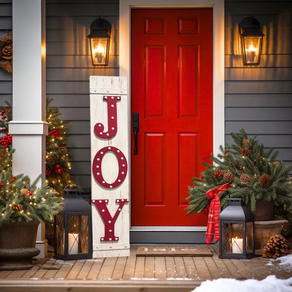 JOY porch leaner sign with red marquee letters leaning against dark red front door with Christmas wreath and gift boxes