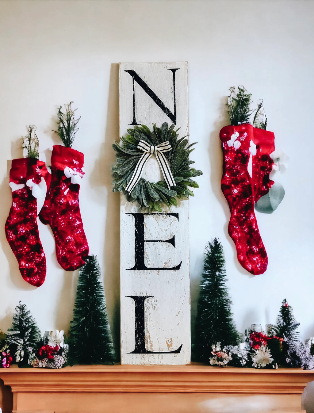 Farmhouse NOEL distressed white wood sign with magnolia wreath and striped bow on white mantel with flocked Christmas tree and silver ornaments
