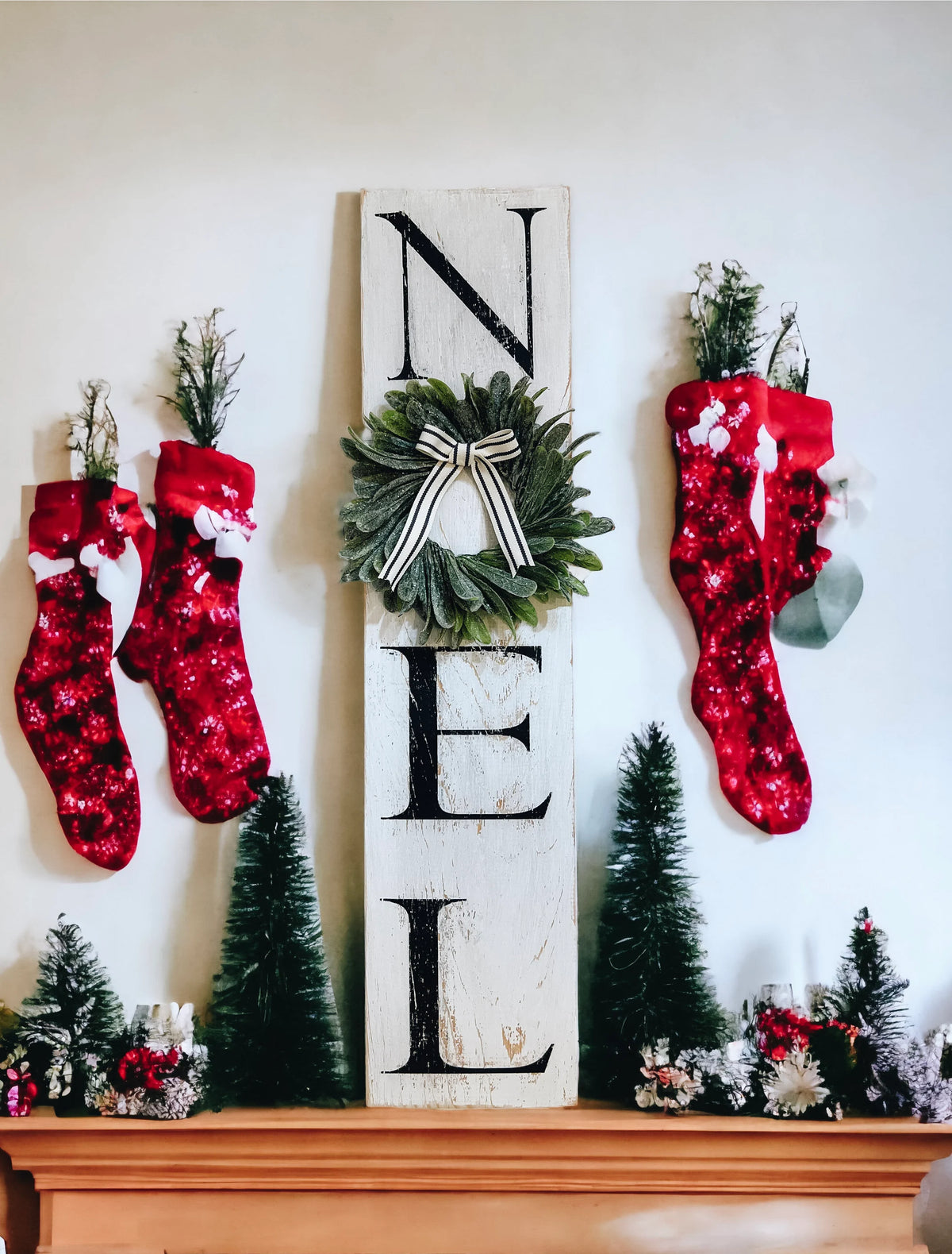Farmhouse NOEL distressed white wood sign with magnolia wreath and striped bow on white mantel with flocked Christmas tree and silver ornaments