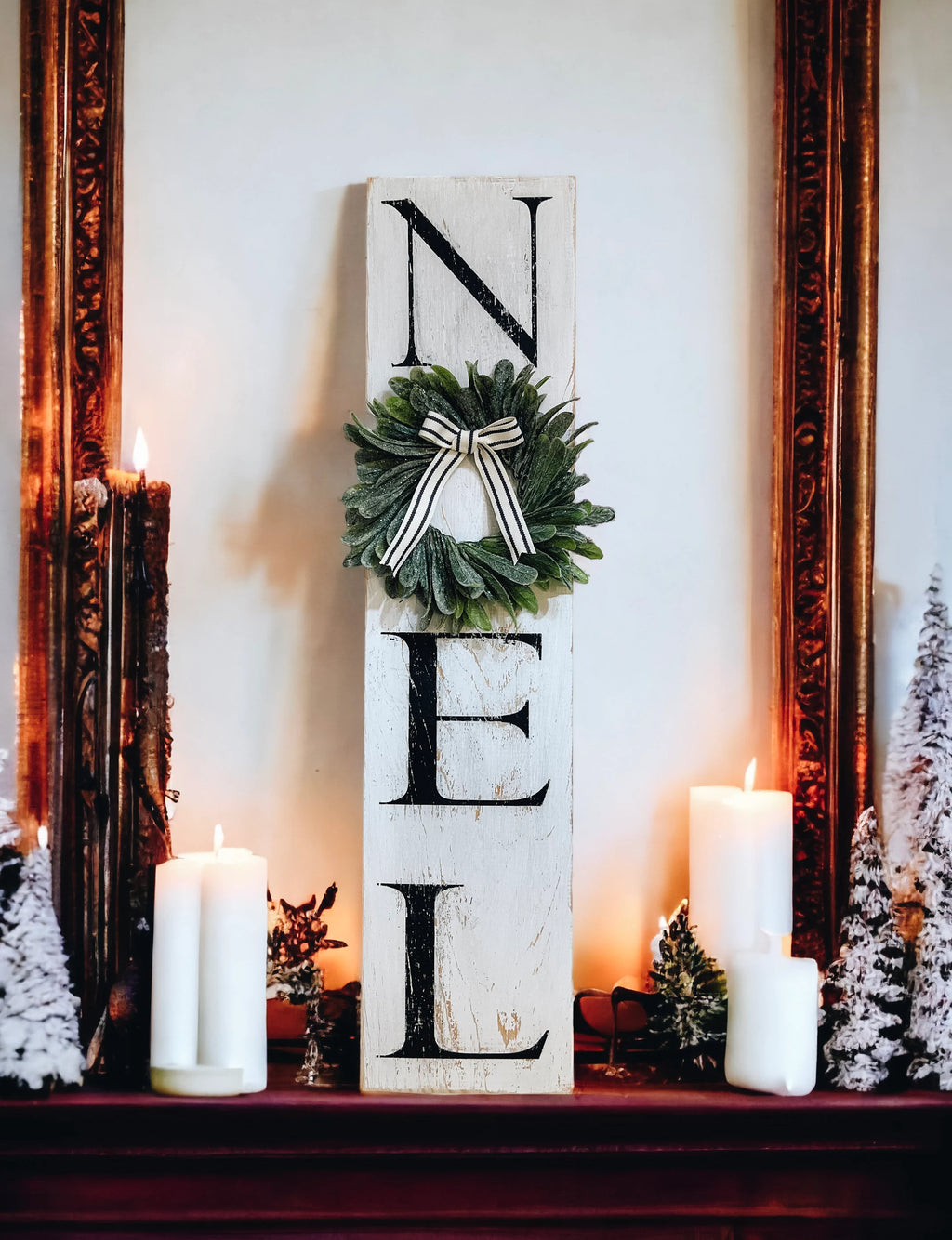 Farmhouse NOEL distressed white wood sign with magnolia wreath and striped bow on white shiplap mantel with lit Christmas tree and pine garland