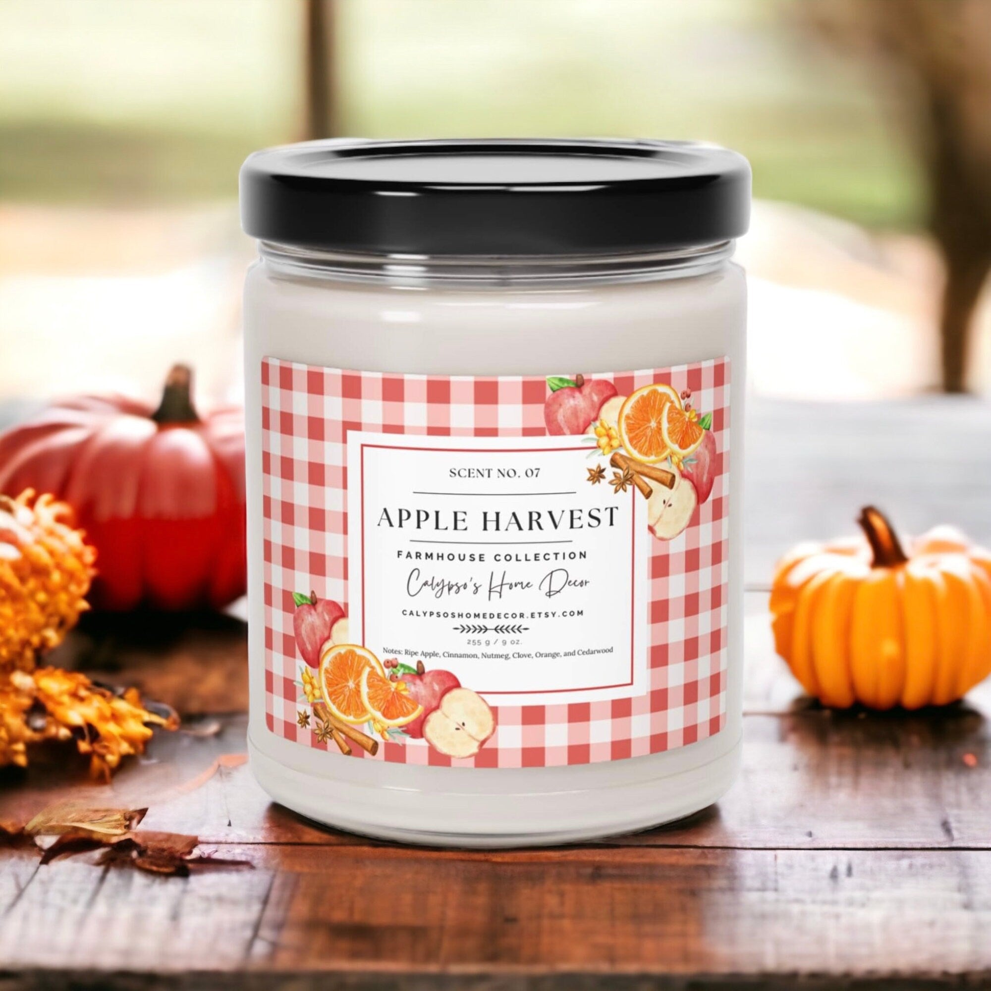 Apple Harvest candle on rustic wood table with orange pumpkins and fall leaves
