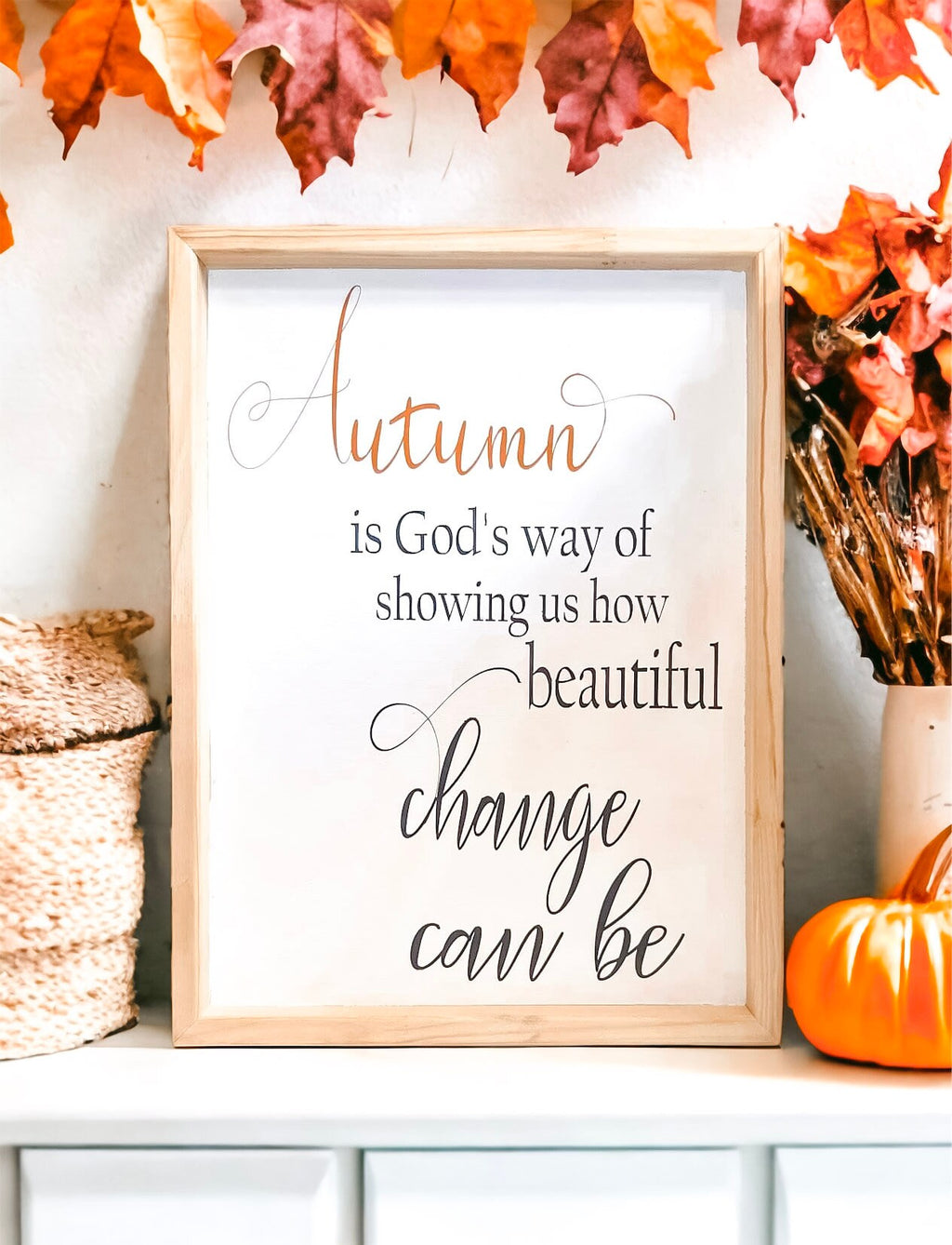 Autumn is Gods Way framed wood sign with copper and black lettering in whitewashed birch frame on white mantel with fall leaf garland and orange pumpkin close up