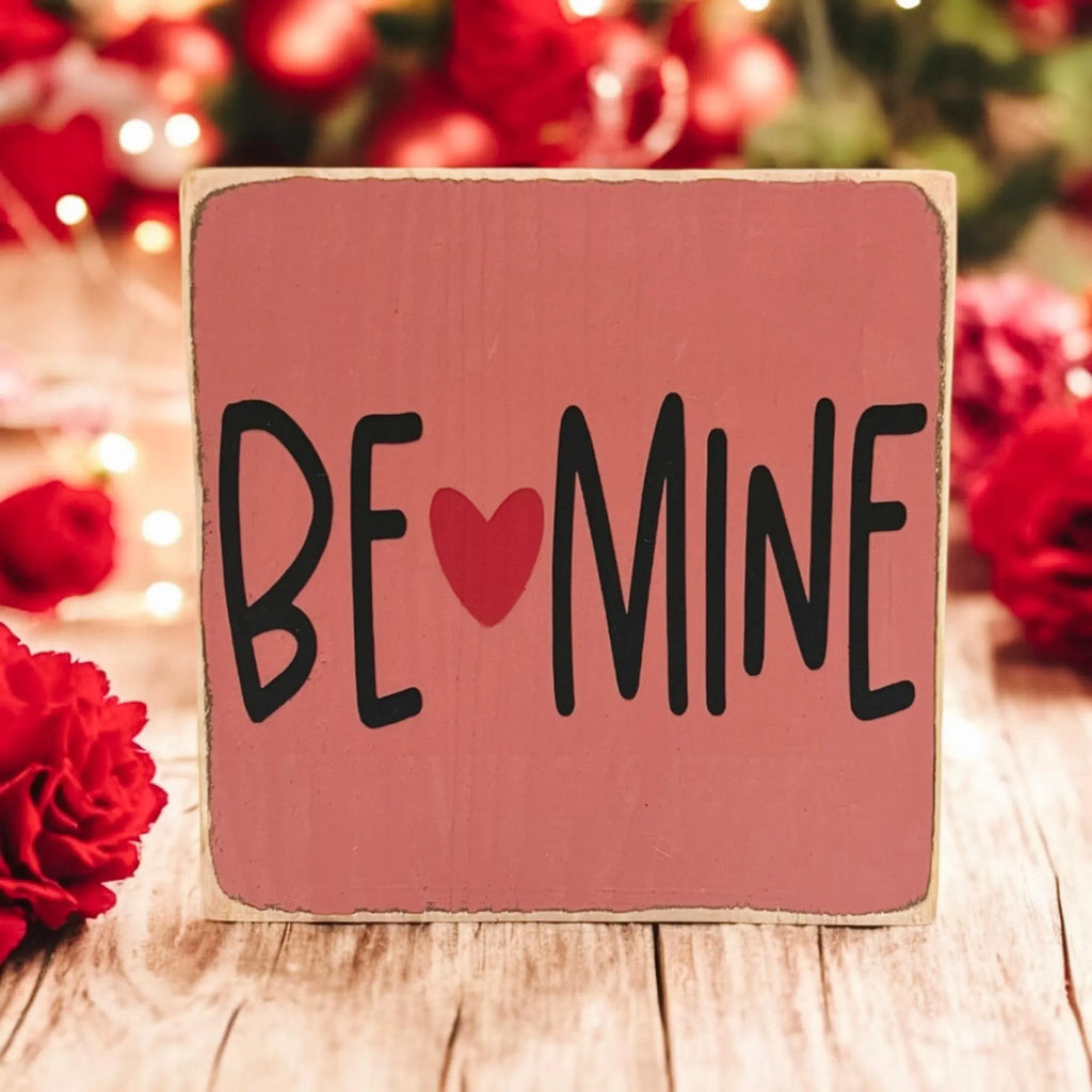 Be Mine Valentine wood block sign on white wood surface with red heart balloons and bokeh lights