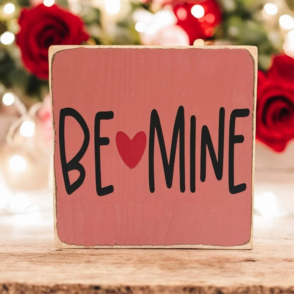 Be Mine Valentine wood block sign on white wood surface with pink and red roses and bokeh lights