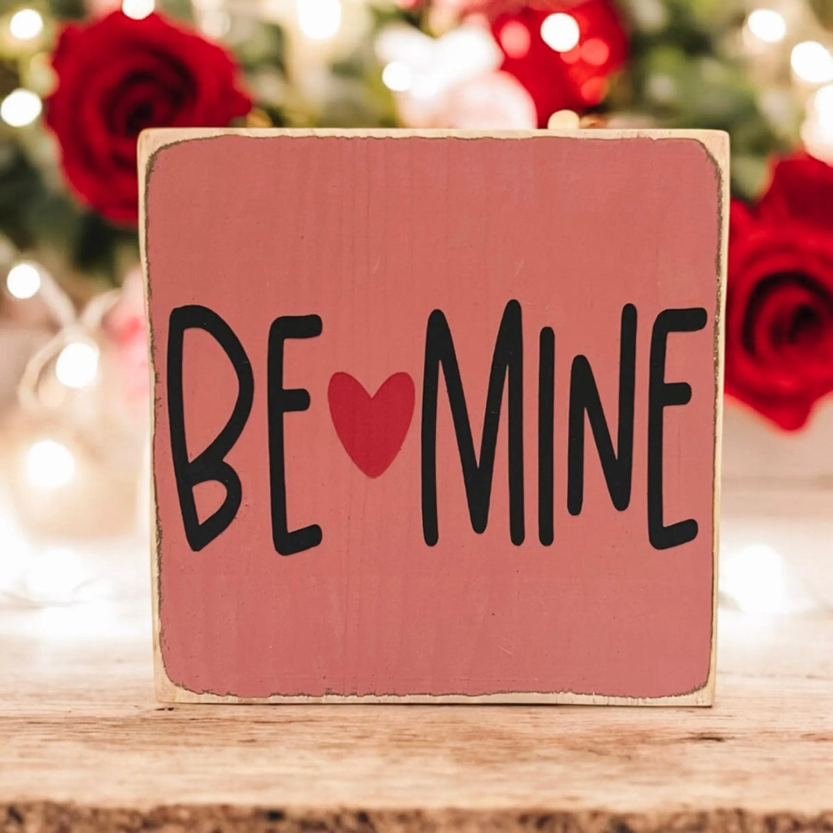 Be Mine Valentine wood block sign on white wood surface with pink and red roses and bokeh lights