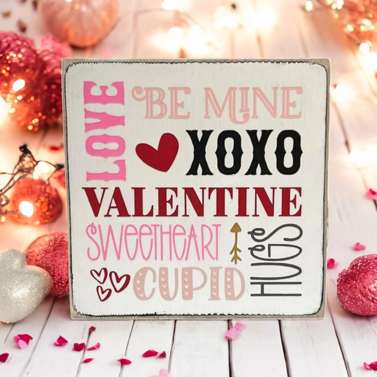 Valentine sayings wood block sign with Love Be Mine XOXO Valentine Sweetheart Cupid Hugs in pink crimson and black on white pine on white shiplap surface with pink roses and warm window light