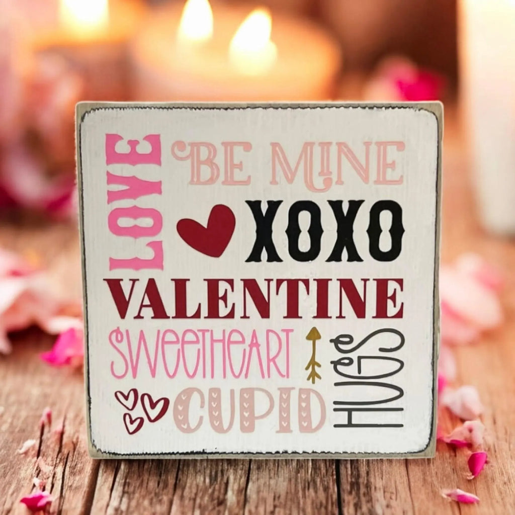 Valentine sayings wood block sign with Love Be Mine XOXO Valentine Sweetheart Cupid Hugs in pink crimson and black on white pine on white wood surface with pink glitter hearts and string lights