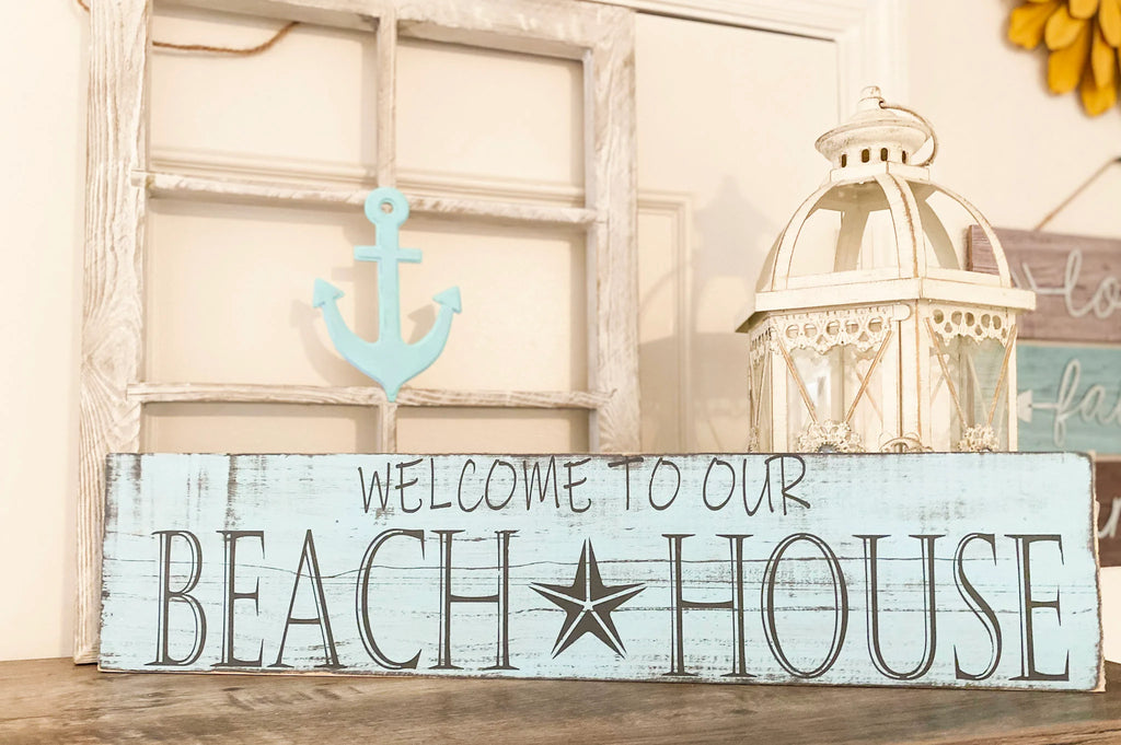 Welcome to Our Beach House reclaimed wood sign leaning against tree trunk close up angled view