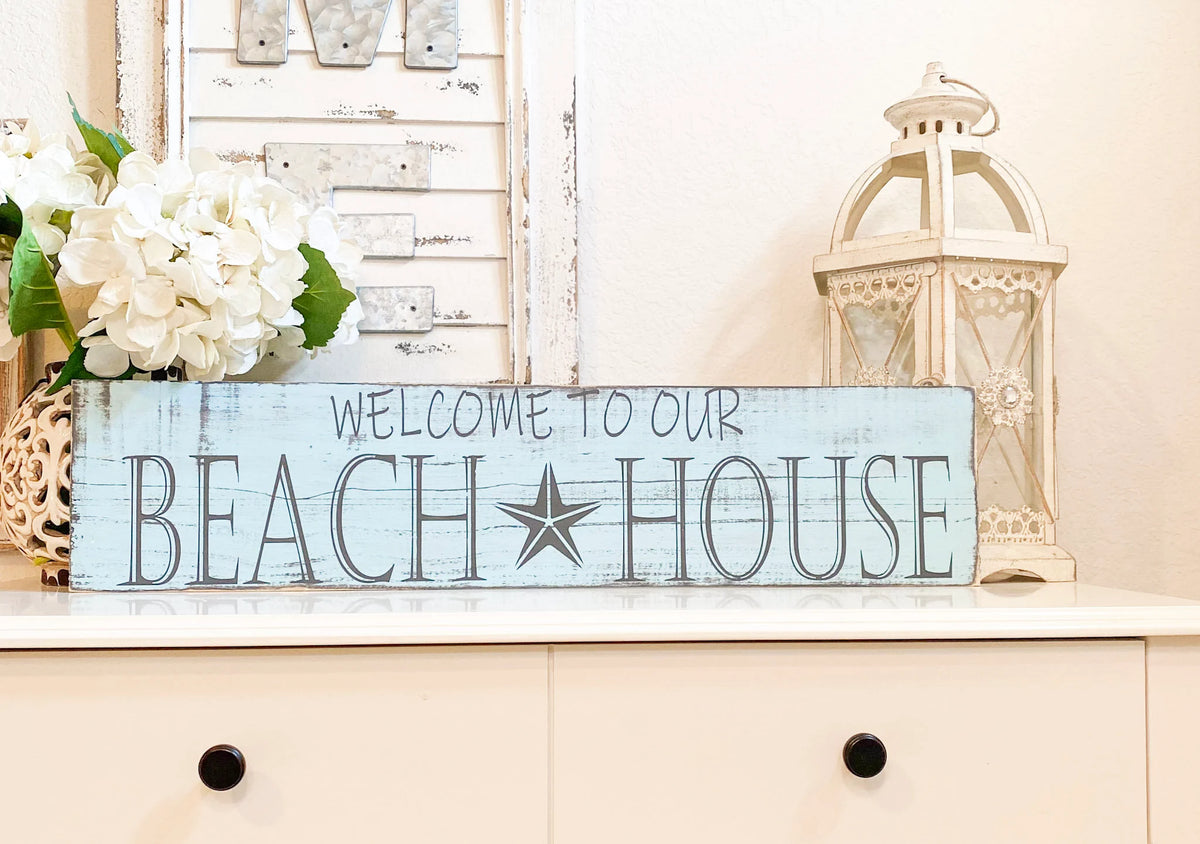 Welcome to Our Beach House reclaimed wood sign leaning against tree trunk full view in natural light