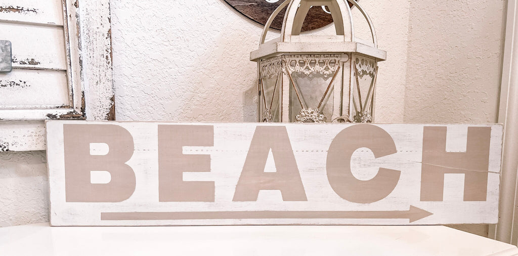 Reclaimed wood Beach arrow sign in distressed white with sandy taupe lettering on white console table with vintage lantern and glass float close up