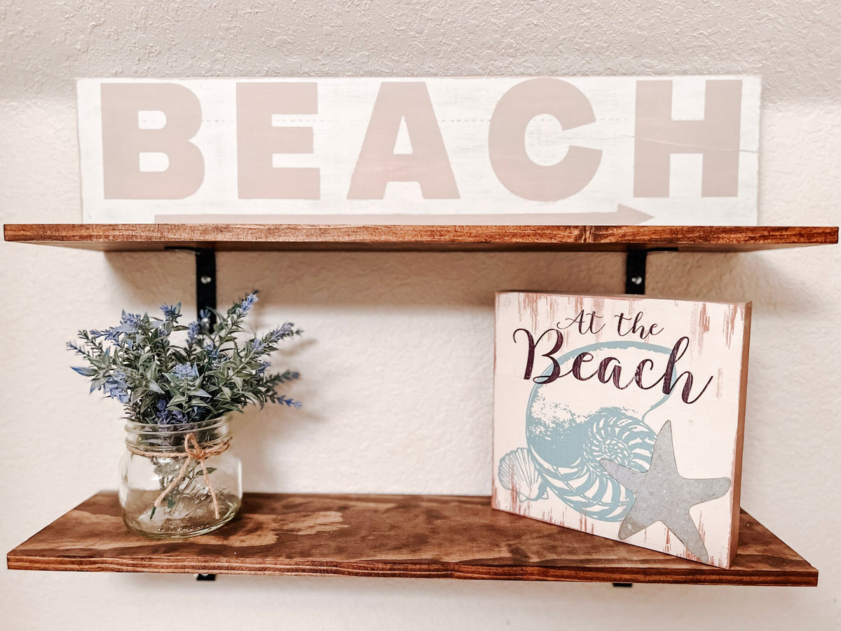 Reclaimed wood Beach arrow sign in distressed white with sandy taupe lettering on rustic wood shelf with At the Beach block sign and mason jar with lavender