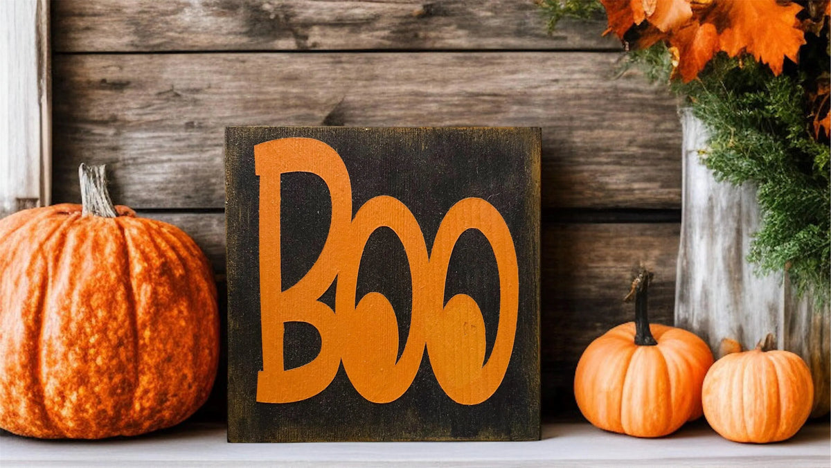 Boo black wood block sign with orange lettering on rustic wood porch shelf with large orange pumpkins and fall foliage