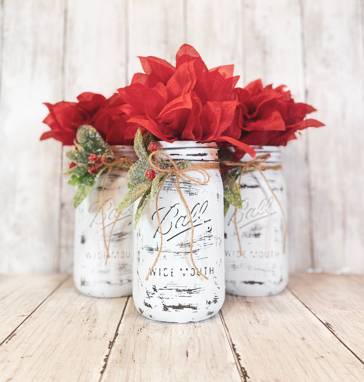 Three farmhouse mason jars with red poinsettia bushes styled on table