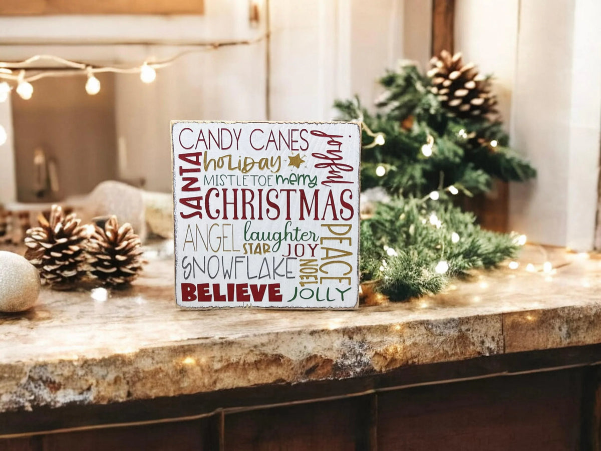 Christmas Favorites word block sign on white countertop with gold and silver ornaments and pine garland close up front view