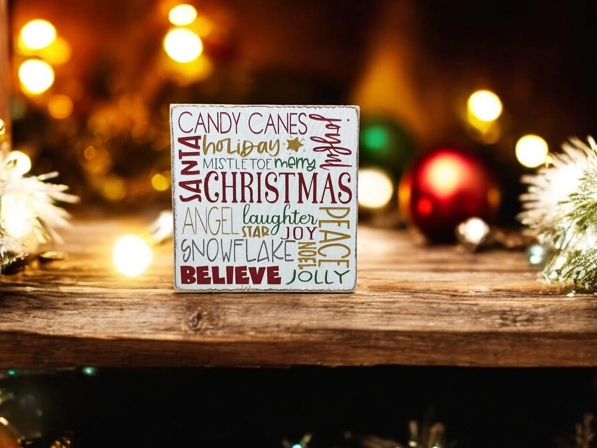 Christmas Favorites word block sign on white countertop with gold and silver ornaments and pine garland wide lifestyle shot