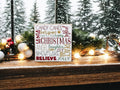 Christmas Favorites word block sign on rustic wood surface with pine cones and lit pine garland in warm light