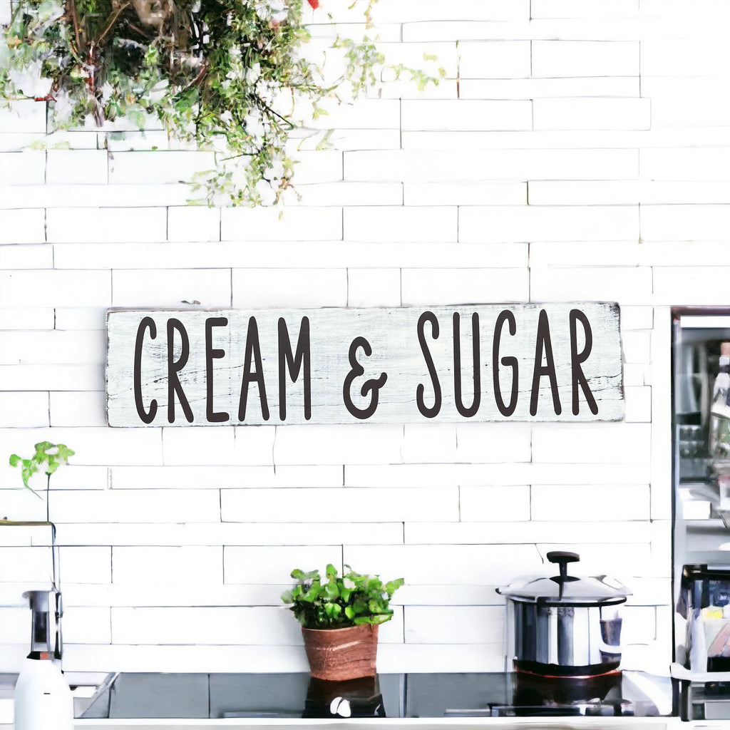 Cream and Sugar distressed white farmhouse wood sign on white brick kitchen wall with white flowers and copper pot