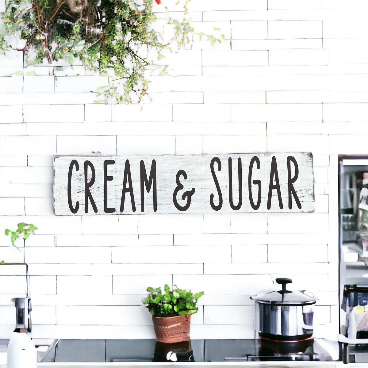 Cream and Sugar distressed white farmhouse wood sign on white brick kitchen wall with white flowers and copper pot