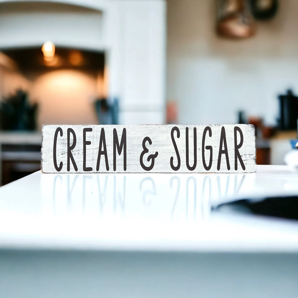 Cream and Sugar distressed white farmhouse wood sign on rustic wood surface with red apple and white ceramic jars close up