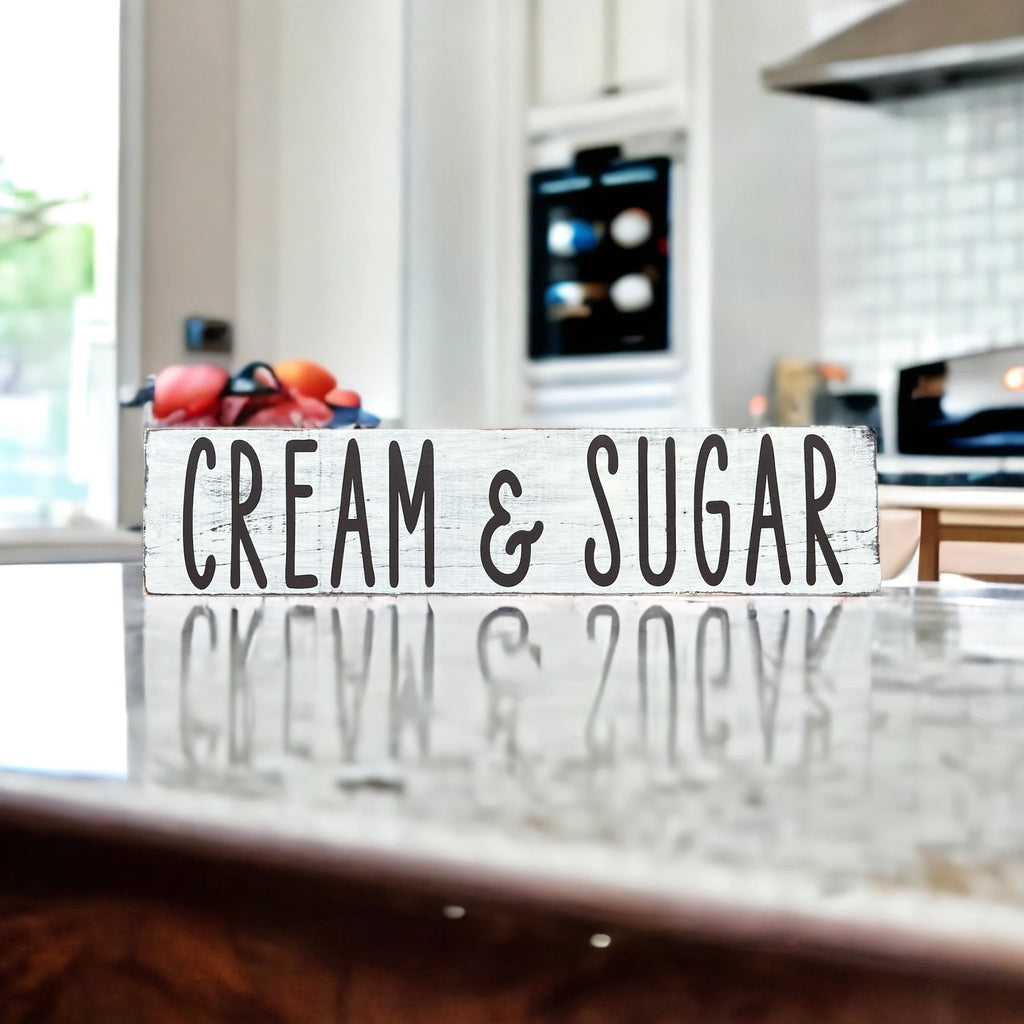 Cream and Sugar distressed white farmhouse wood sign on rustic wood surface with red apple and white ceramic jars in background
