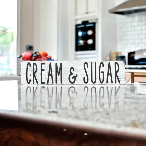 Cream and Sugar distressed white farmhouse wood sign on rustic wood surface with red apple and white ceramic jars in background