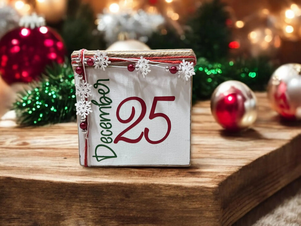 December 25 Christmas wood block sign with red 25 and green December script jute top and snowflake bead garland on round wood slice with red and silver ornaments and pine sprigs