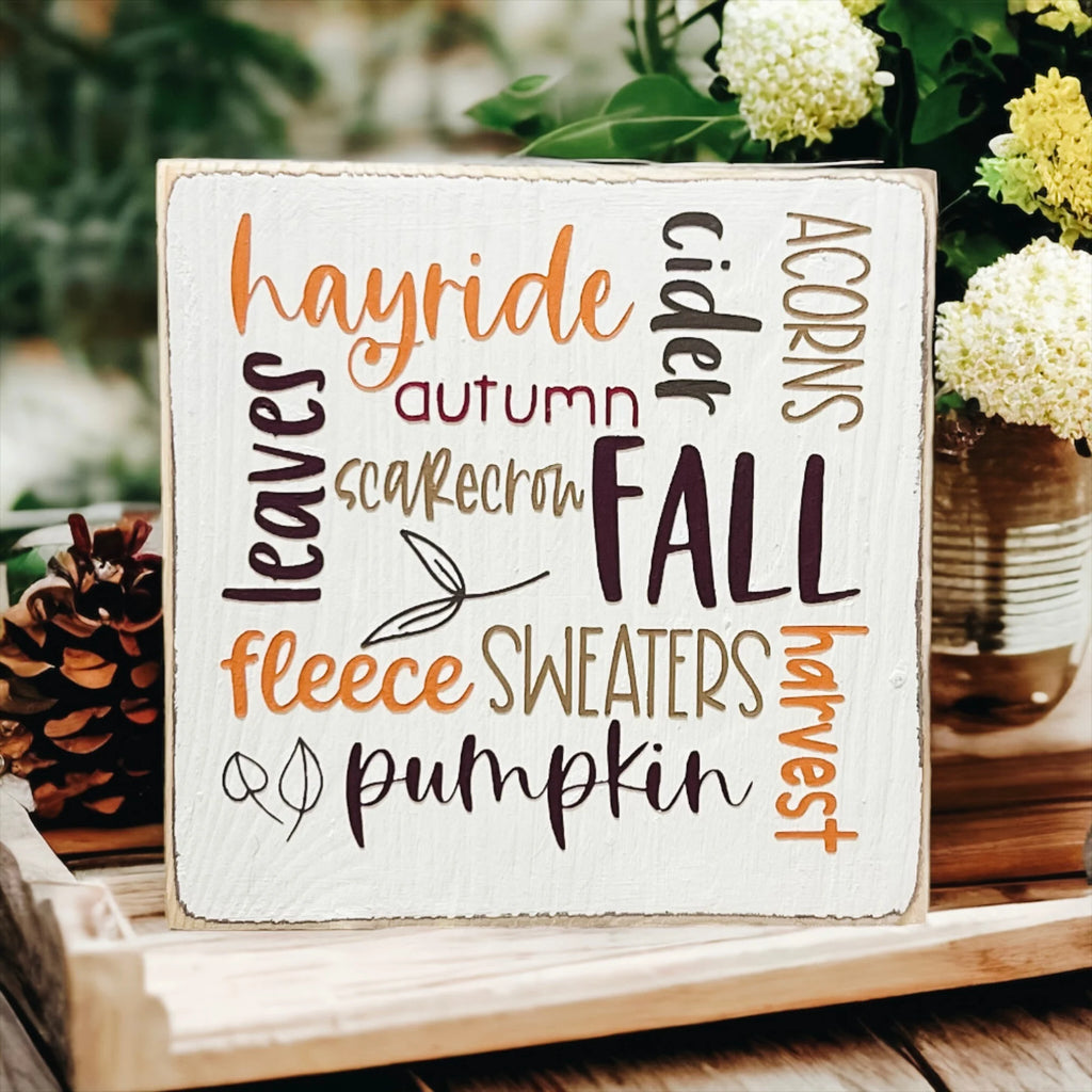 Fall Favorites word cloud wood block sign on white wood surface with pine cones close up