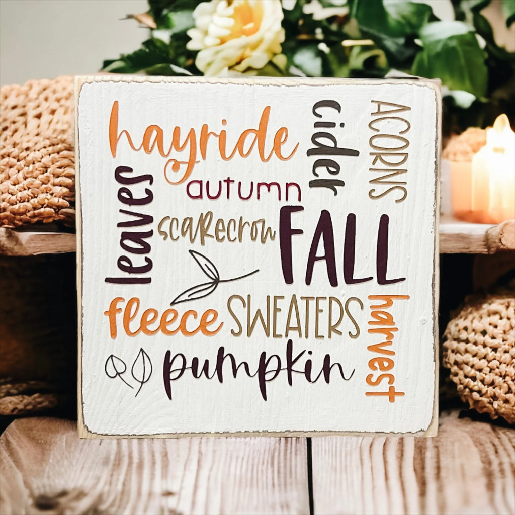 Fall Favorites word cloud wood block sign on white wood surface with yellow flower and pine cone