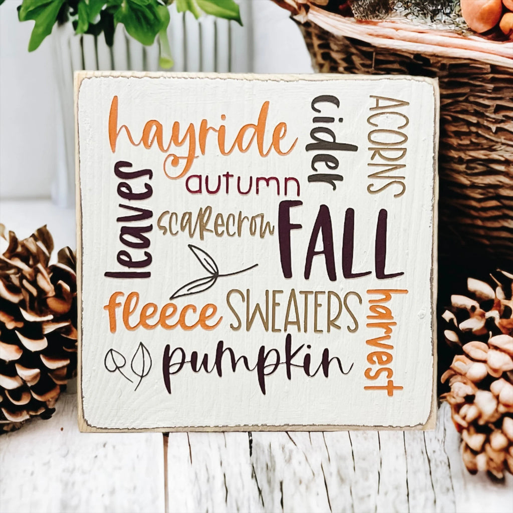 Fall Favorites word cloud wood block sign on white wood surface with autumn leaves and small pumpkin in background