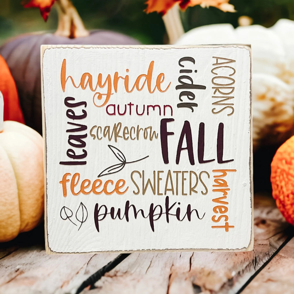 Fall Favorites word cloud wood block sign on wood tray with pine cone and white hydrangeas in background
