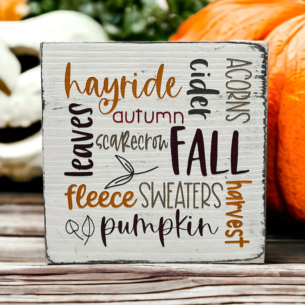 Fall Favorites word cloud wood block sign on white wood surface with pine cones and wicker basket in background