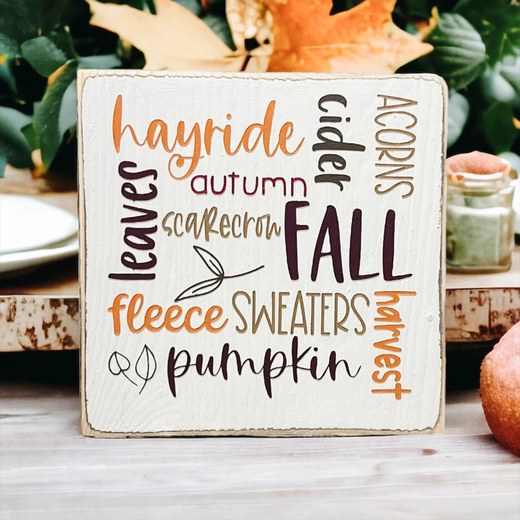Fall Favorites word cloud wood block sign on wood dining table with autumn leaf and pear in foreground