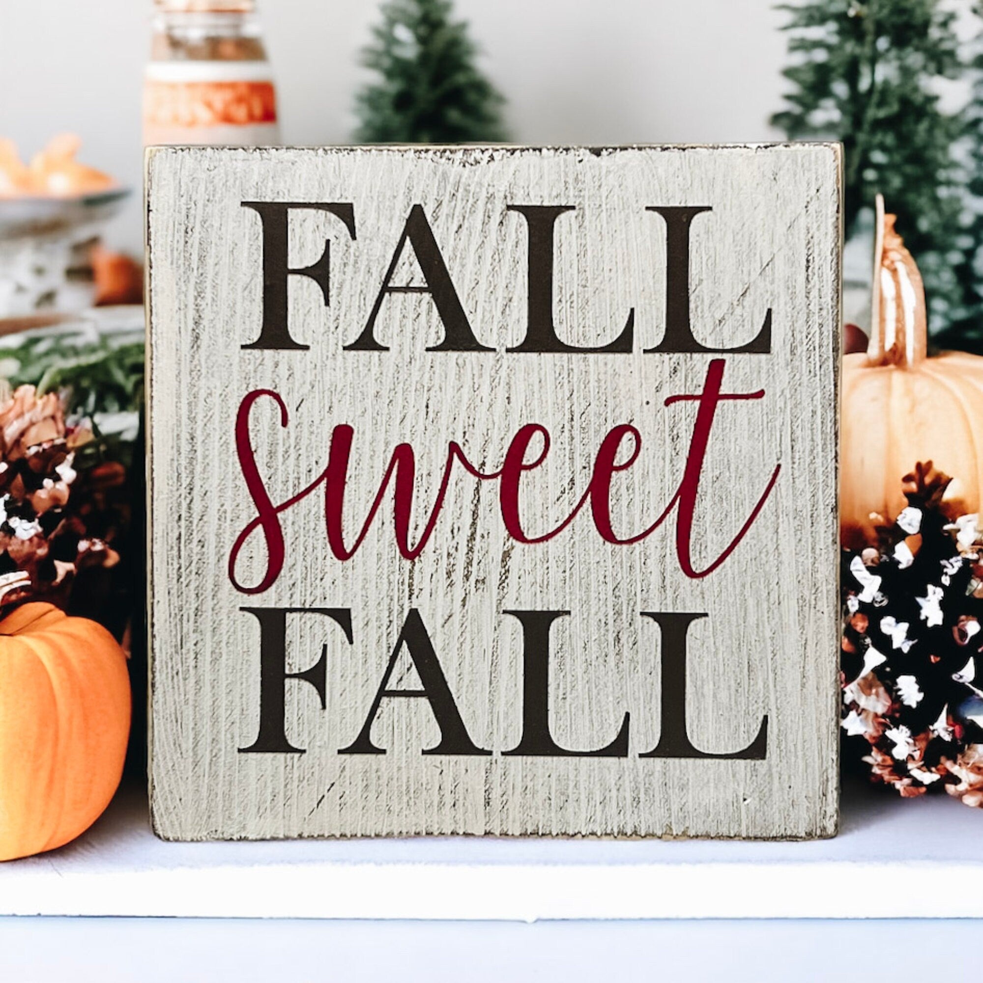 Fall Sweet Fall distressed white wood block sign on rustic wood table with orange pumpkins and fall leaves close up