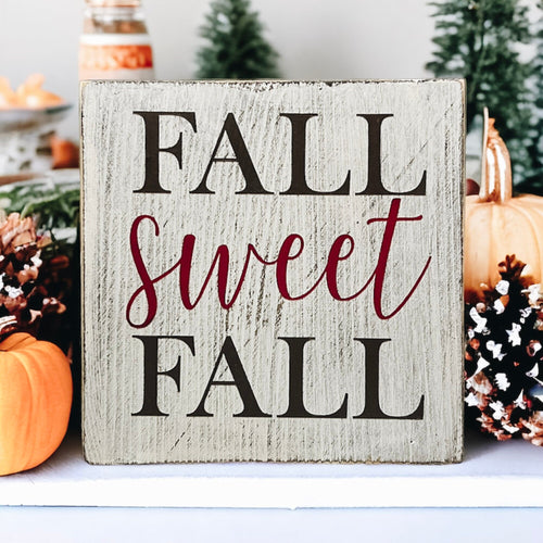 Fall Sweet Fall distressed white wood block sign on rustic wood table with orange pumpkins and fall leaves close up