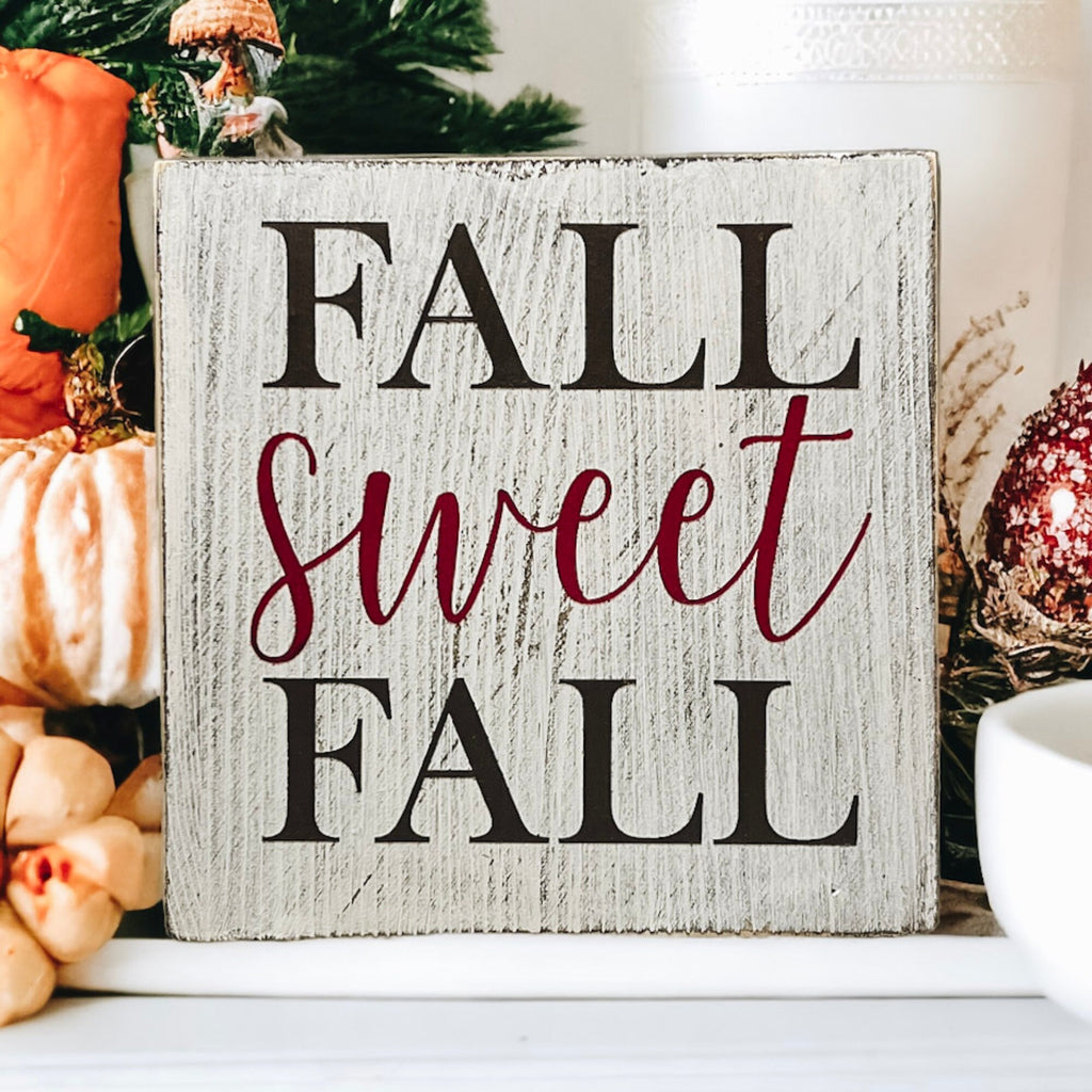 Fall Sweet Fall distressed white wood block sign on rustic wood table with orange pumpkins and fall leaves wide view