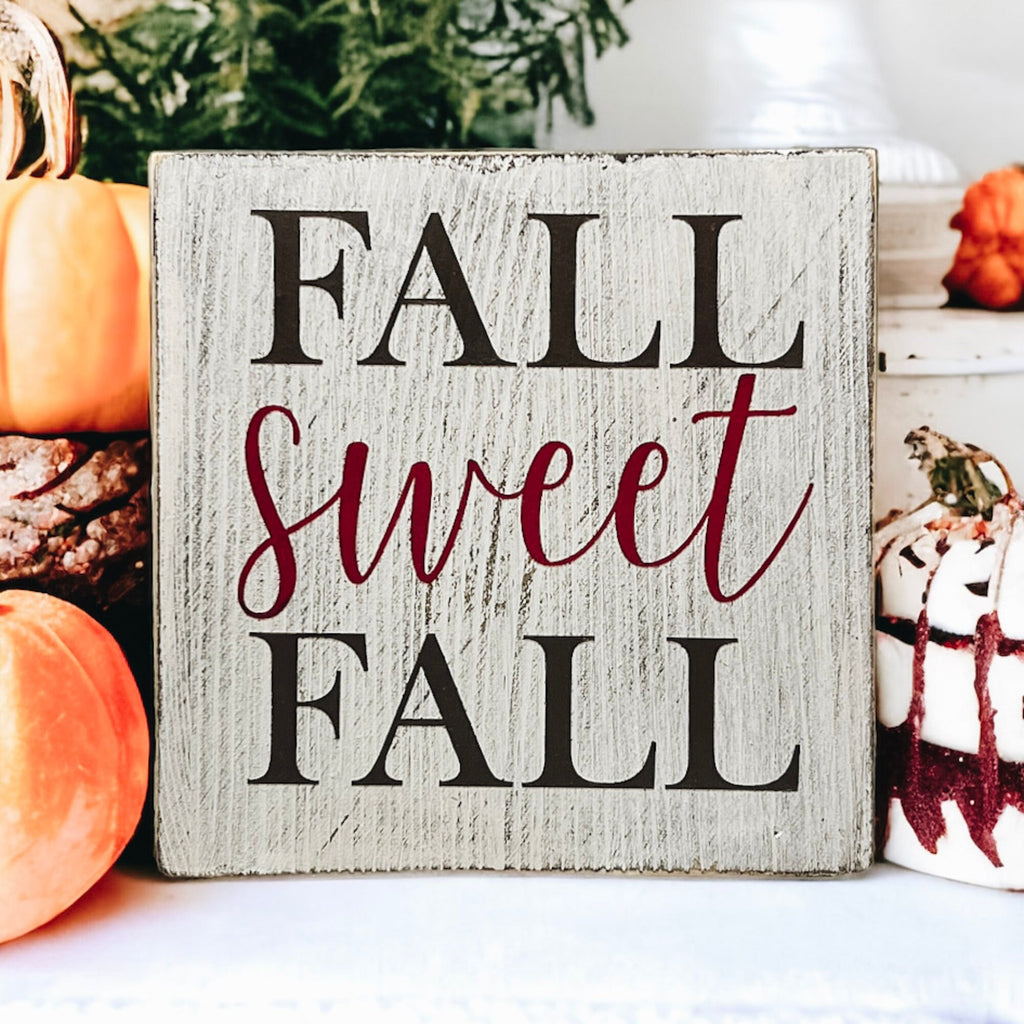 Fall Sweet Fall distressed white wood block sign on rustic wood surface with dried botanicals and orange pumpkins