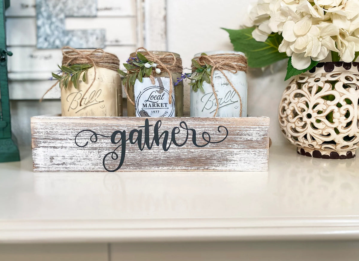 Three painted farmhouse mason jars with jute and greenery in whitewashed Gather tray on white surface
