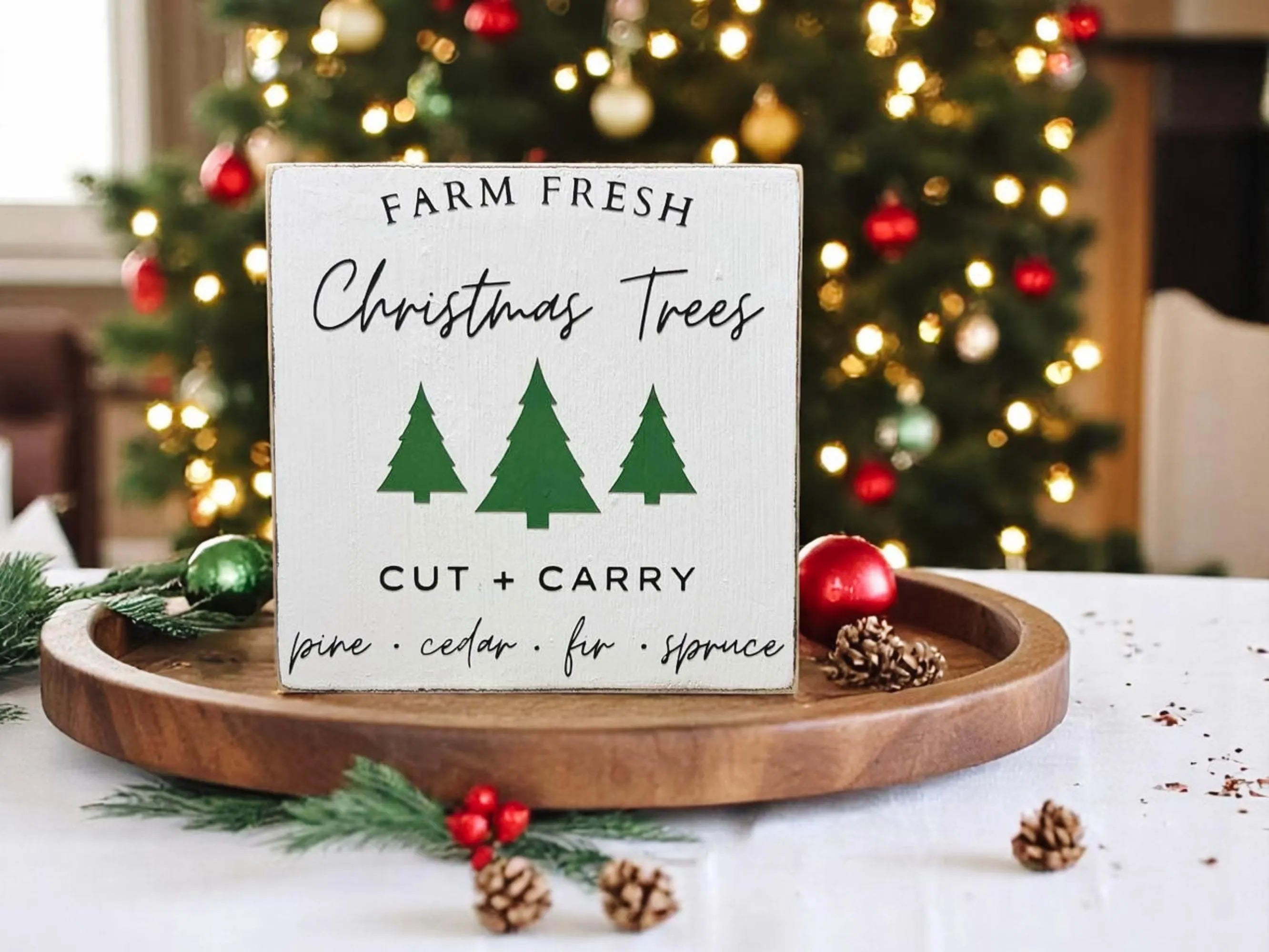 Farm Fresh Christmas Trees wood block sign on round wood tray with red and green ornaments and pine sprigs
